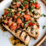 Juicy Bruschetta Chicken topped with fresh tomatoes, basil, and balsamic glaze on a white plate.