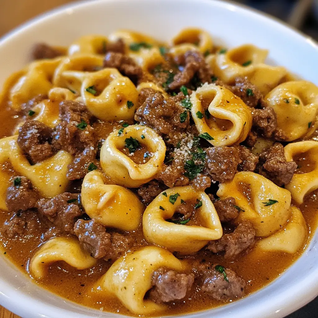 Cheesesteak Tortellini in a creamy cheese sauce, topped with sautéed peppers and steak, served in a white bowl.