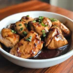 A close-up of Crockpot Bourbon Chicken coated in a thick, glossy bourbon sauce, served on a plate with a side of stir-fried vegetables.