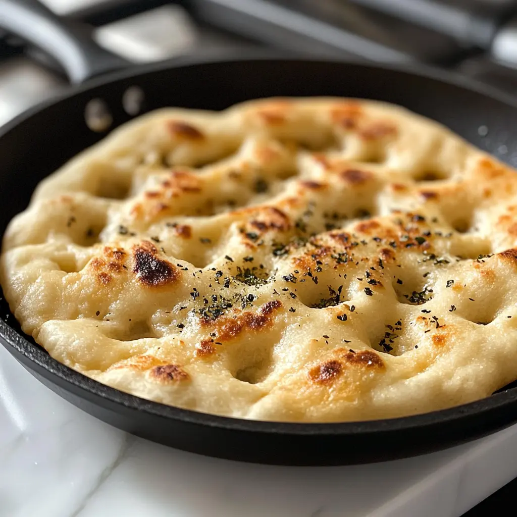 A golden-brown Parmesan Focaccia Bread with a crispy crust, sprinkled with fresh herbs and cheese, on a wooden cutting board.